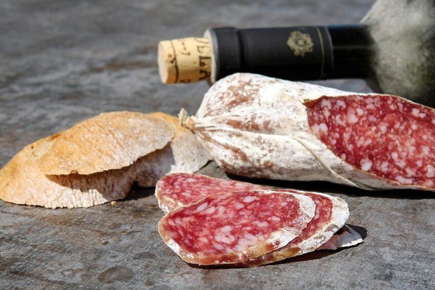 Una hogaza de pan, lonchas de salami y una botella de vino sobre una superficie de piedra. 5