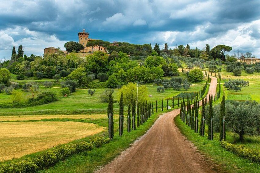Un camino de tierra que lleva a un edificio histórico en una colina, rodeado de campos verdes y árboles. 2