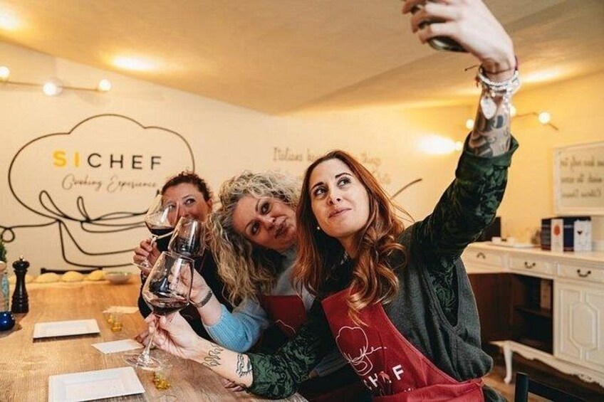 Tres personas tomándose un selfie en un restaurante con un letrero que dice 'SICHEF Cooking Experience'. 1
