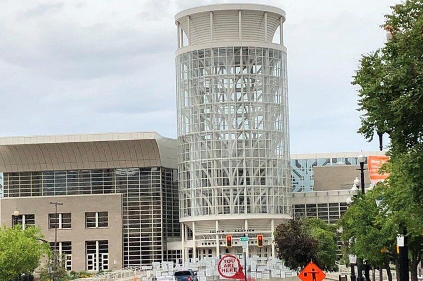 A modern building with a cylindrical glass structure, surrounded by trees and other buildings. 2