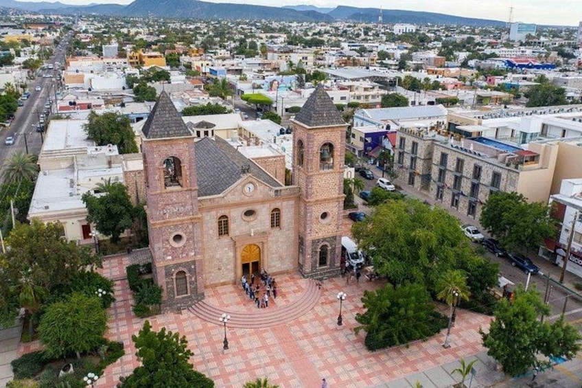 A historic church with a bell tower, surrounded by a plaza with trees and a busy street. 5