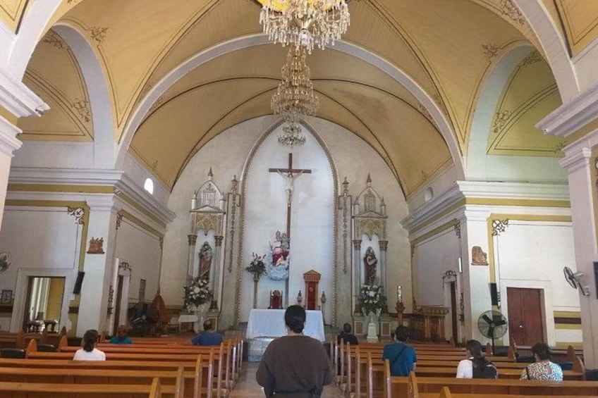 Interior de iglesia con bancas, una araña y estatuas religiosas. 2