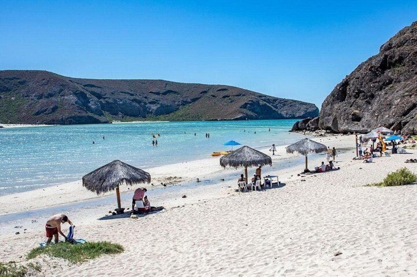 Una playa con gente tomando el sol, sombrillas y un mar azul cristalino. 5