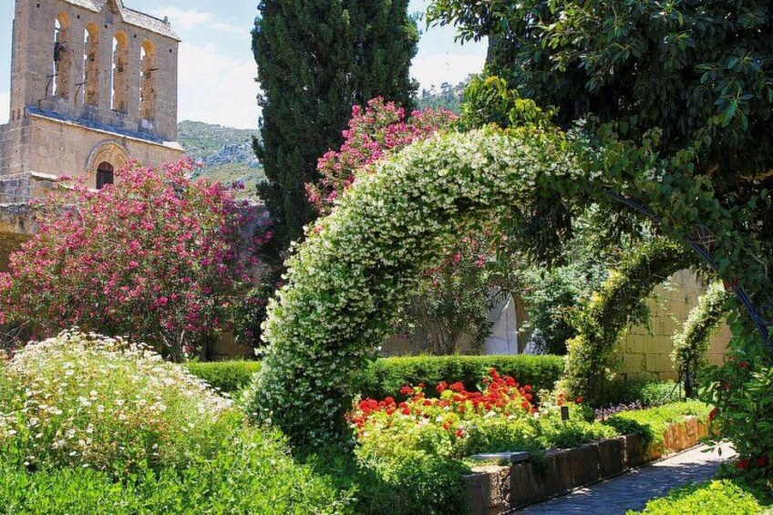 Un jardin agrémenté d’une arche en pierre, de plantes en fleurs et, au fond, d’un bâtiment historique. 2