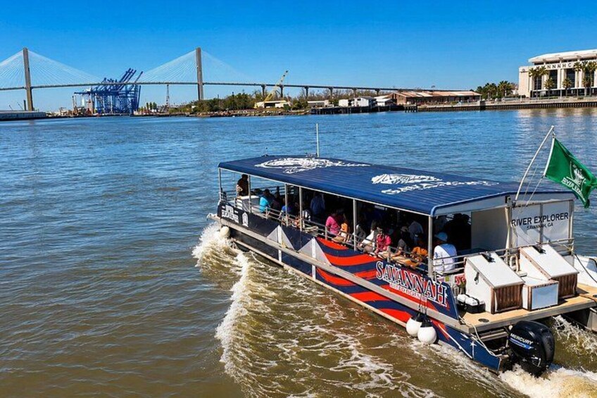 Un barco de crucero fluvial llamado 'River Explorer' con pasajeros, un puente al fondo y una bandera. 2