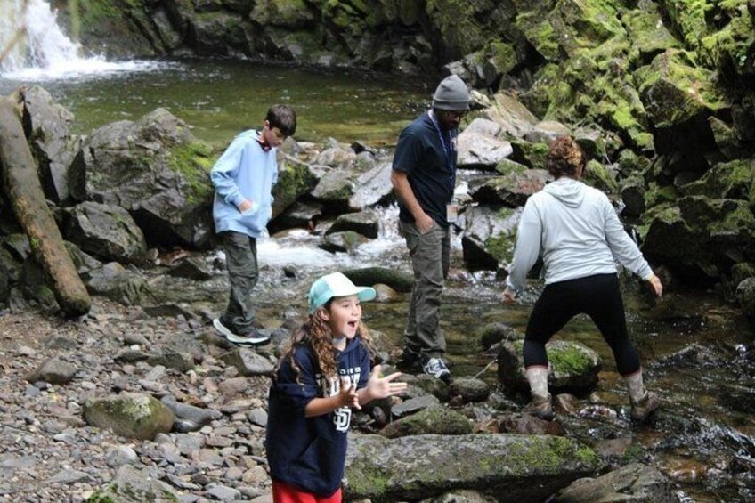 Des personnes se tiennent près d’un ruisseau rocheux, avec une cascade en arrière-plan. 5