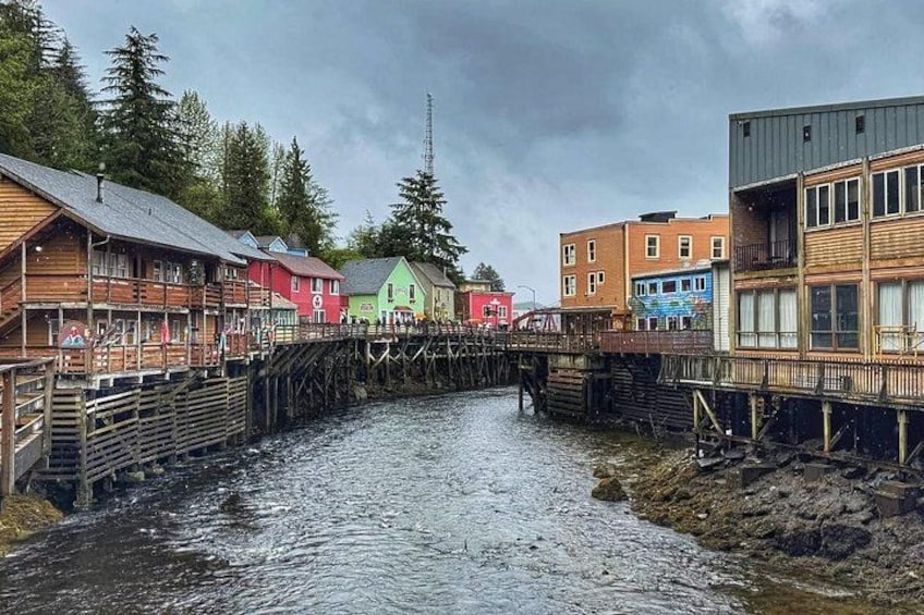 Un pont en bois enjambant une rivière, des bâtiments aux couleurs vives de part et d’autre, et un ciel nuageux. 3