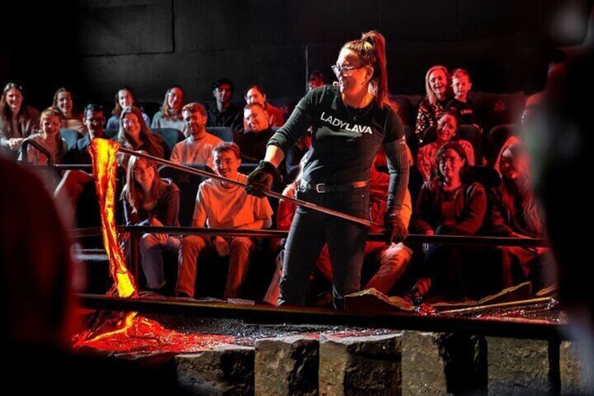 A performer in a black shirt with 'LADYLAVA' on it, standing in a ring with a crowd watching. 5