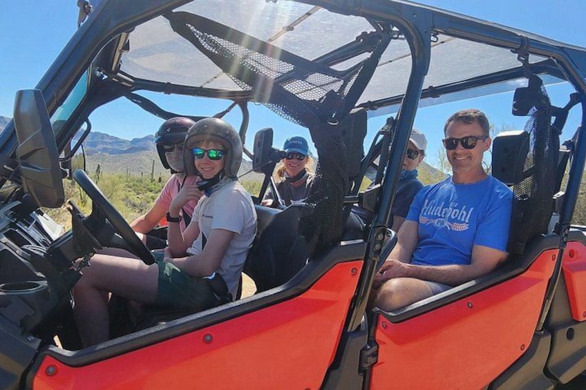 A group of people in a red off-road vehicle with a desert landscape in the background. 5