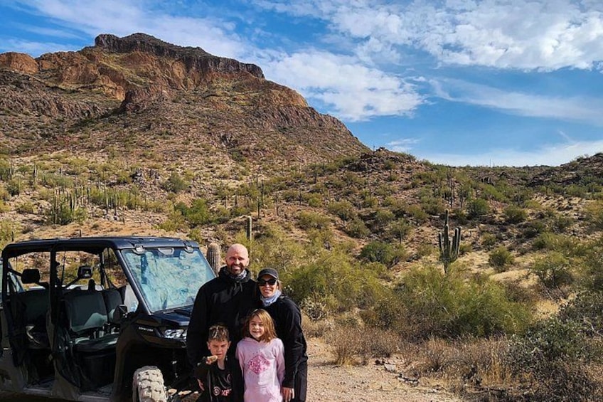 A family posing in front of a desert landscape with a vehicle and a mountain in the background. 3