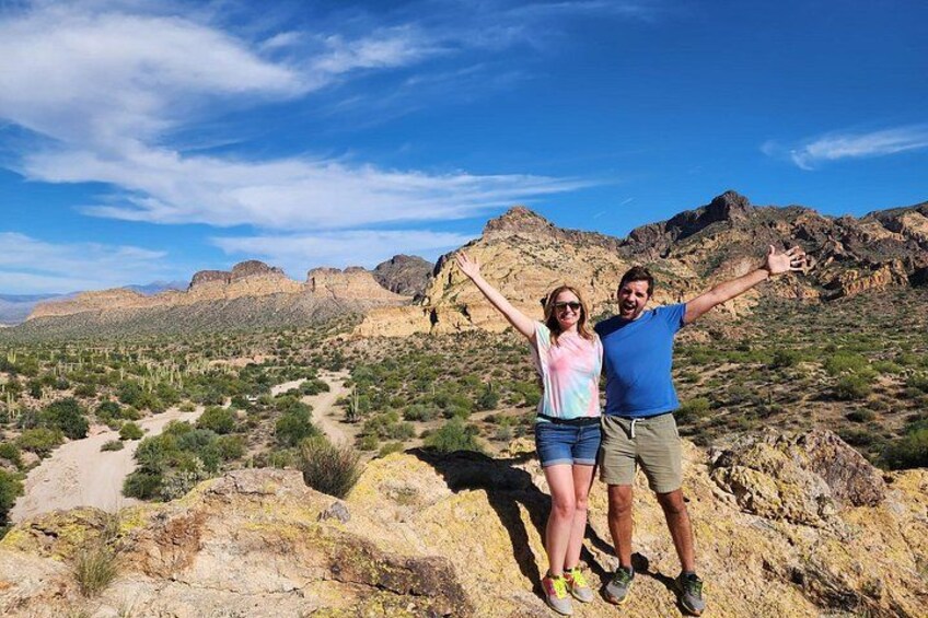 Two people standing on a rocky outcrop with a desert landscape and mountains in the background. 4