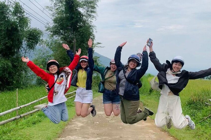 A group of people jumping on a dirt path surrounded by greenery and hills. 3