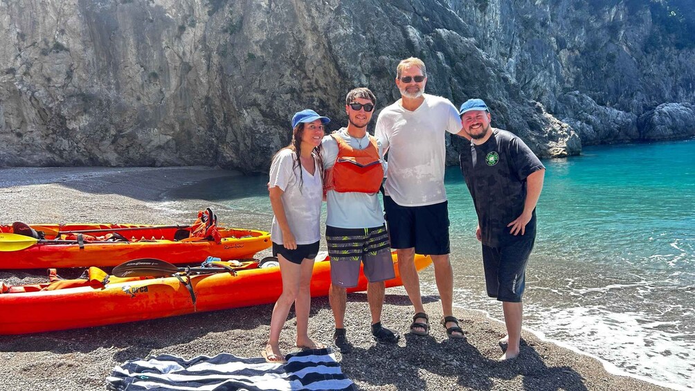 Un gruppo di persone in piedi su una spiaggia rocciosa, con kayak e un mare cristallino sullo sfondo. 5