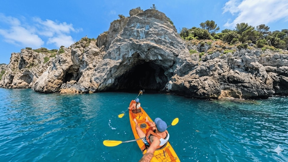 Un kayakista in un kayak giallo pagaia vicino a una costa rocciosa con l'ingresso di una grotta. 1