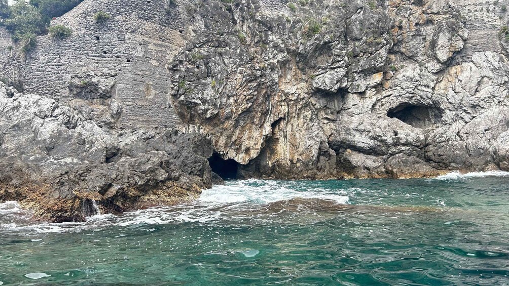 Paesaggio costiero roccioso con l'ingresso di una grotta e un mare agitato. 3