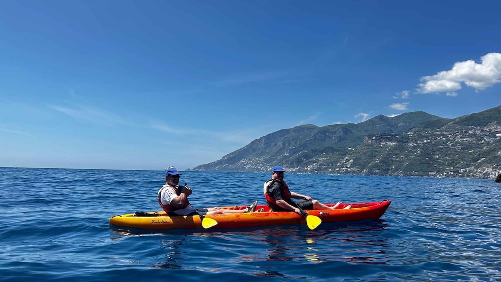 Due persone che fanno kayak su un mare calmo, con una costa montuosa sullo sfondo. 2