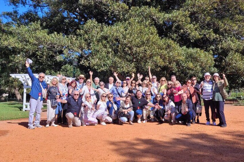 Un gruppo di persone che posano in un parco con alberi e una struttura bianca sullo sfondo. 2