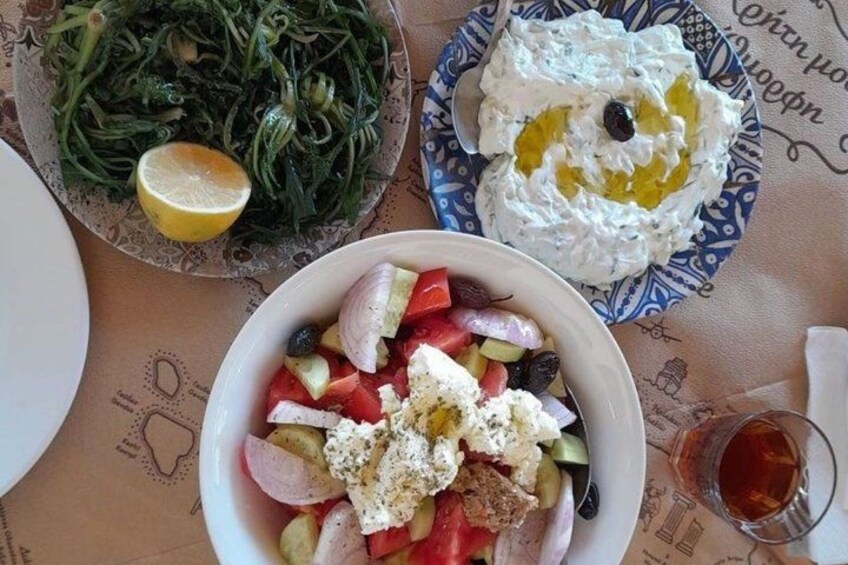 A table with a salad, a bowl of yogurt with olive oil, and a plate of greens. 3