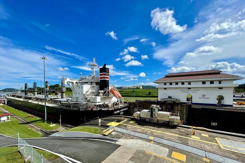 Een groot vrachtschip afgemeerd in een haven, met een wit gebouw op de achtergrond waarop 'Global Shipping Panama' staat. 3