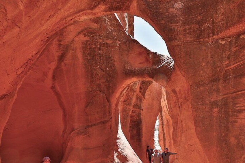 A red rock canyon with a narrow passageway and a group of people standing at the end. 5