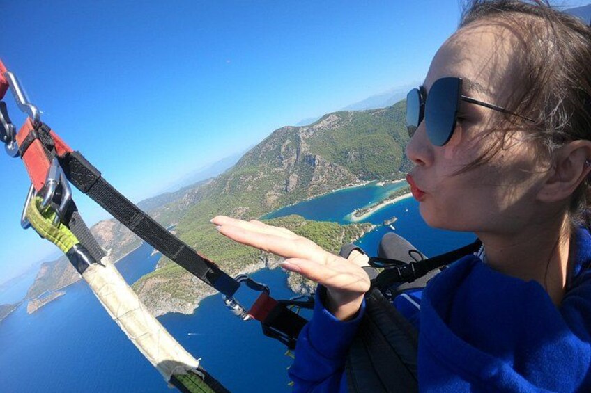 Una persona haciendo bungee jumping con arnés y equipo de seguridad, con vistas a un paisaje costero con montañas y una masa de agua. 4
