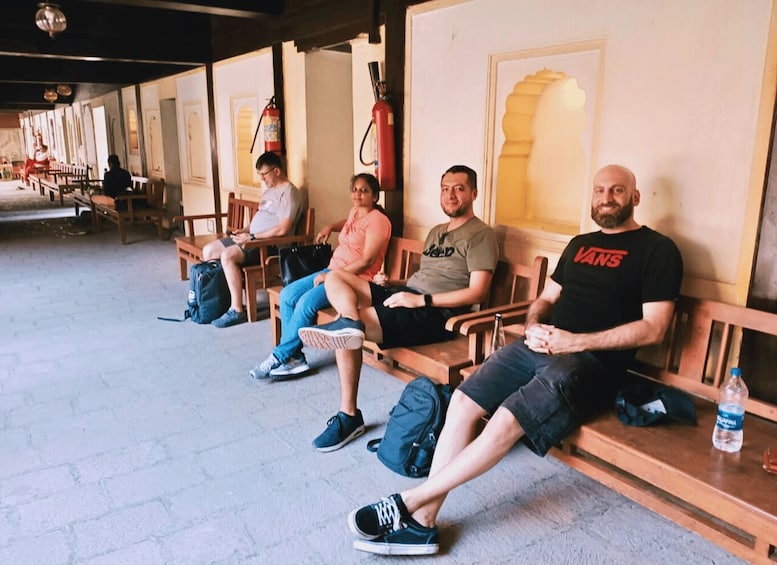 A row of wooden benches with people sitting, a fire extinguisher on the wall, and a water bottle on the bench. 2