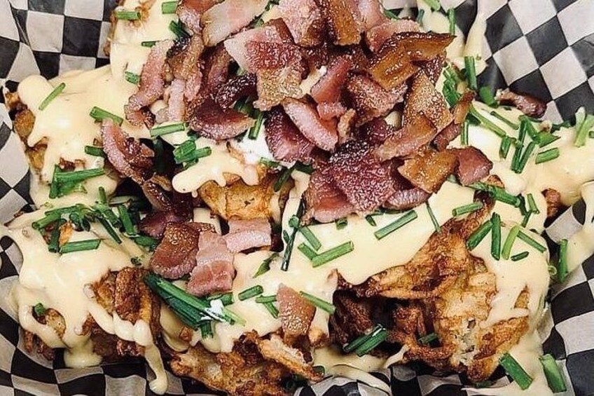 A dish of fried potatoes topped with crispy bacon and chives, served in a paper container. 4
