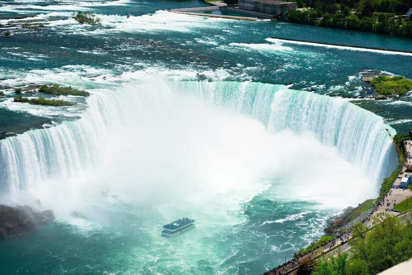 Ein großer Wasserfall mit einem Boot im Wasser, umgeben von viel Grün und einem Gebäude in der Ferne. 4