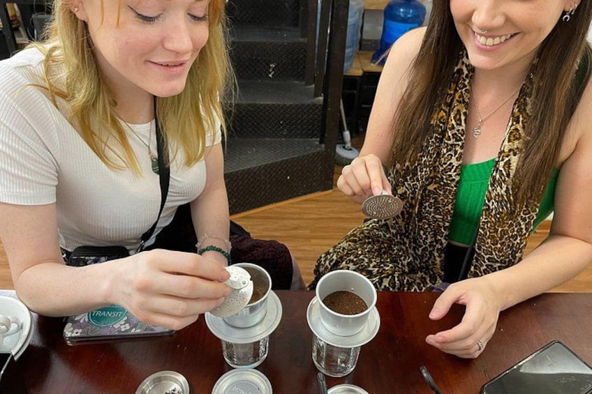 Dos mujeres sentadas en una mesa con tazas de café y un molinillo. 3