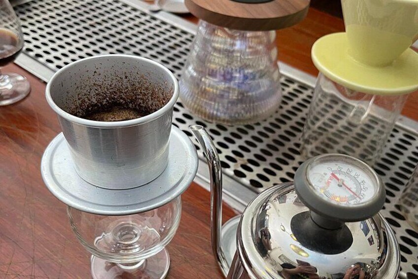 Een metalen koffiepotje op een schotel, een glazen karaf en een koffiepers op een tafel. 4