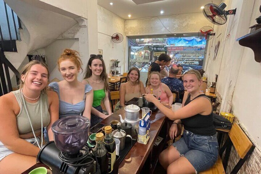 Een groep mensen zit aan een tafel in een café, met een blender en verschillende drankjes erop. 5
