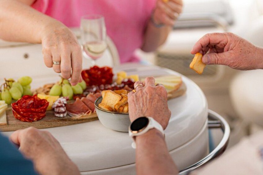 A group of people at a table with a variety of cheeses, fruits, and bread. 2