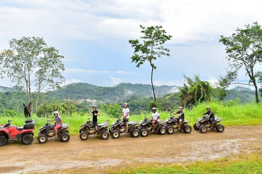 A group of people on quad bikes on a dirt road with green grass and trees in the background. 5