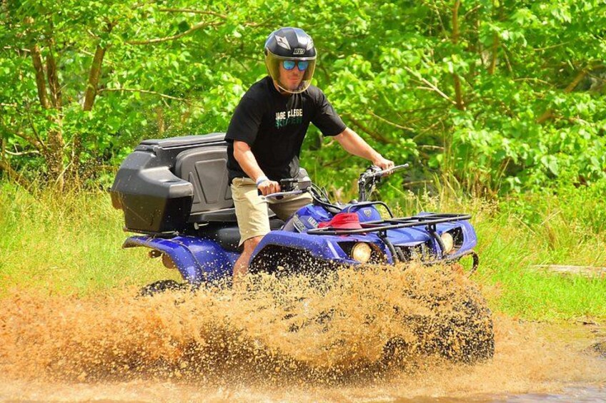 A person riding a blue ATV on a dirt road surrounded by greenery. 1