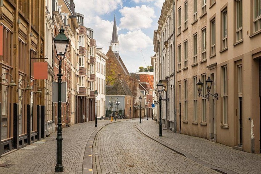 A cobblestone street lined with historic buildings, a church steeple, and street lamps. 2