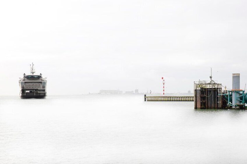 A ferry moving across a foggy body of water, approaching a dock with industrial structures. 4