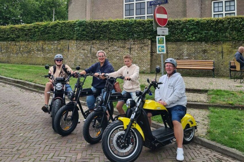 Four people on electric scooters, a brick pathway, a hedge, and a no entry sign. 2