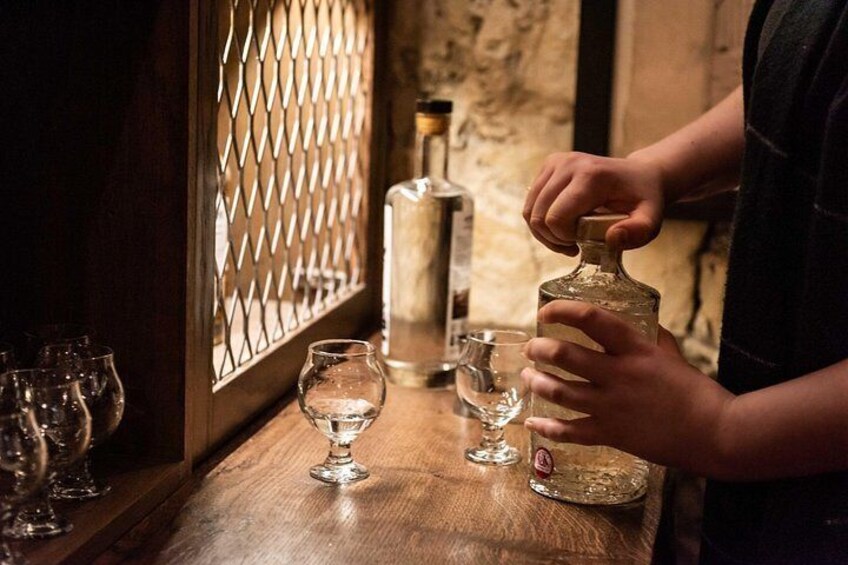 Una persona sirve un líquido de una botella a un vaso sobre una barra de bar de madera. 3