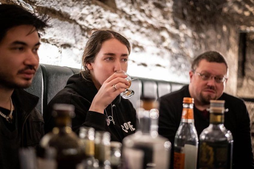 Iemand drinkt uit een glas, zittend aan een tafel met flessen. 3