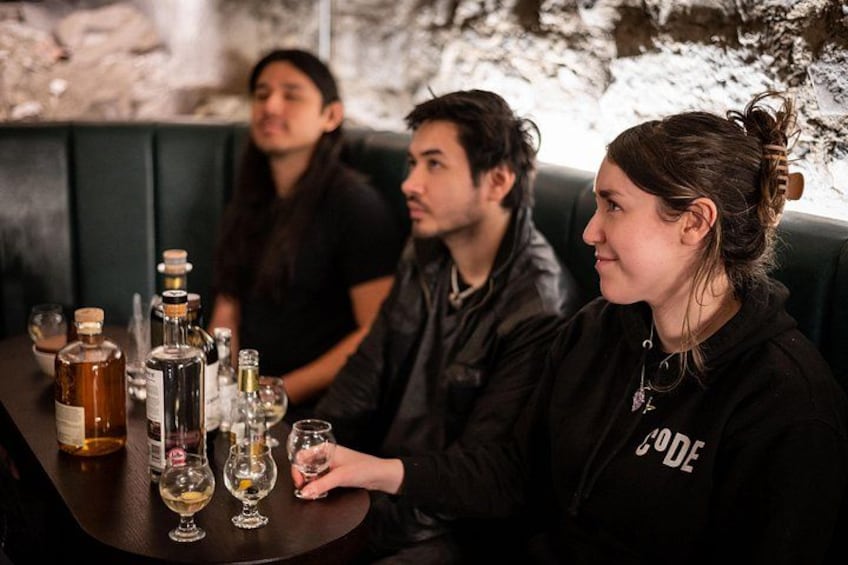 Een groep mensen zit aan een tafel met verschillende flessen en glazen, vermoedelijk in een bar of restaurant. 2