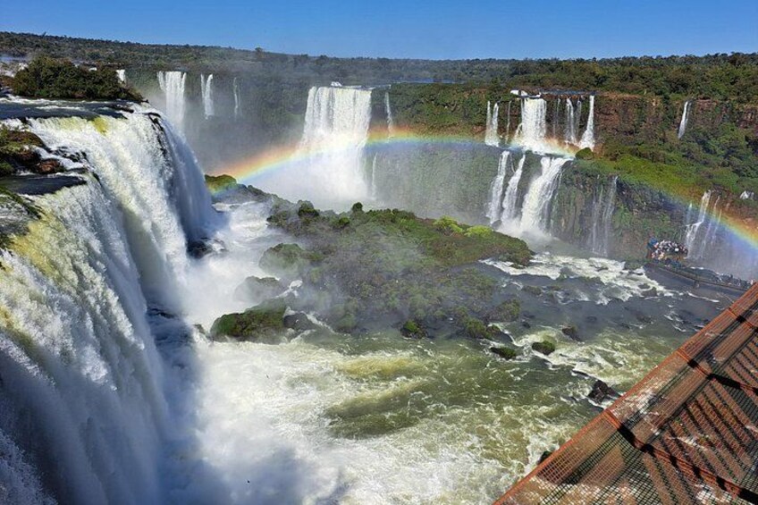 A waterfall with a rainbow, lush greenery, and a boat in the foreground. 2