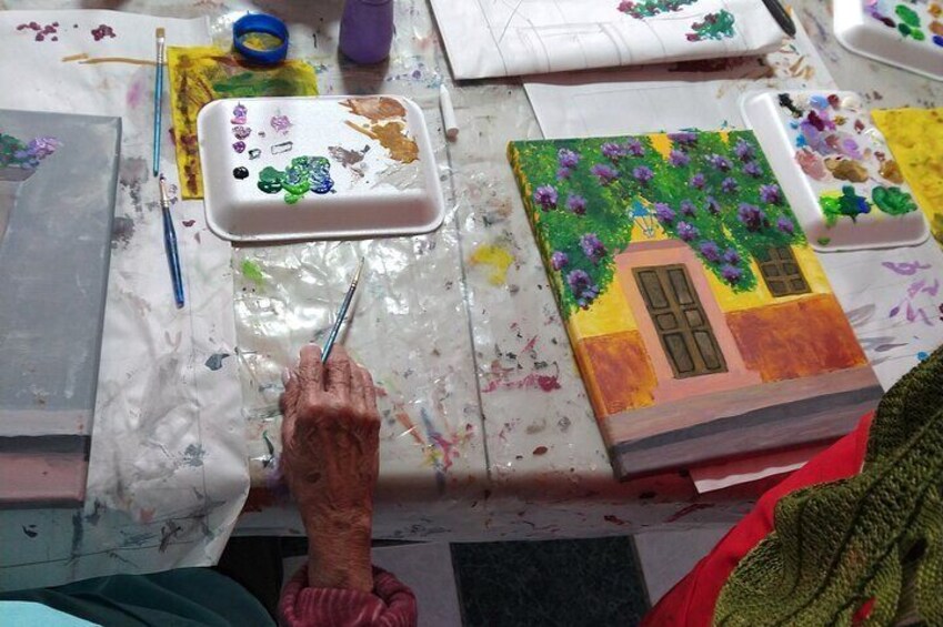 An artist painting a house with purple flowers on a canvas. 5