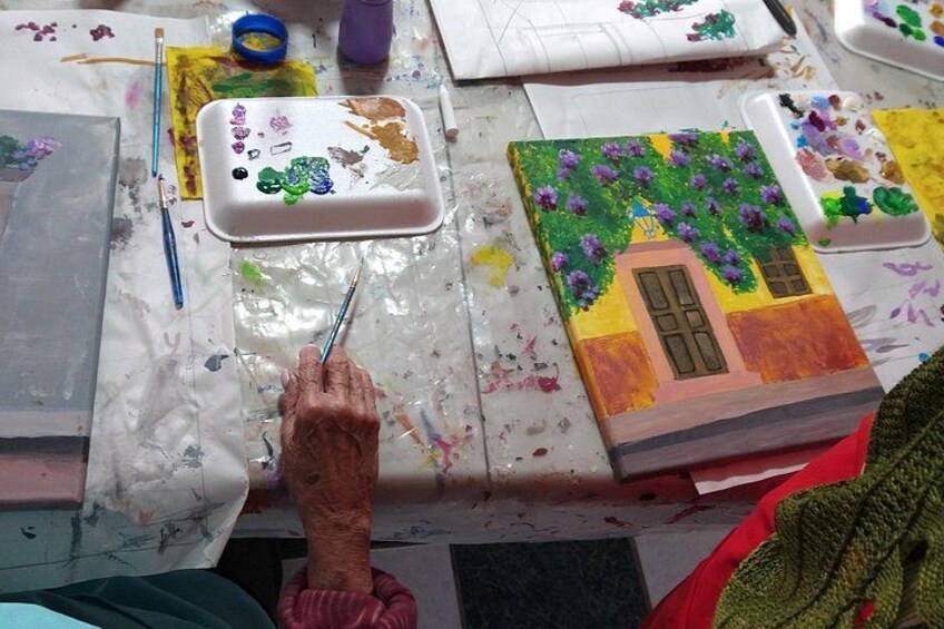 A person painting a house with purple flowers on a table covered with paint splatters. 5