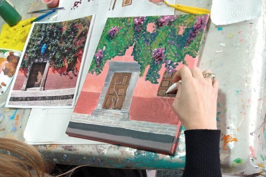 A person painting a house with a door and window, surrounded by paintbrushes and paint. 3
