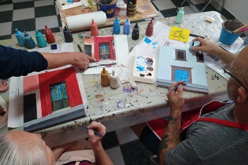 A person painting a model house with various colors and tools on a table. 2