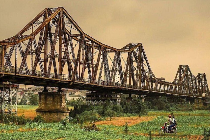 A large, rusted bridge spanning a river with a person riding a motorcycle on the far side. 3