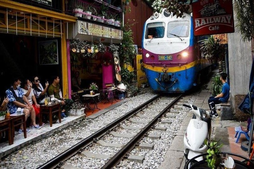 Un tren sobre rieles, una cafetería y personas sentadas en el exterior. 1