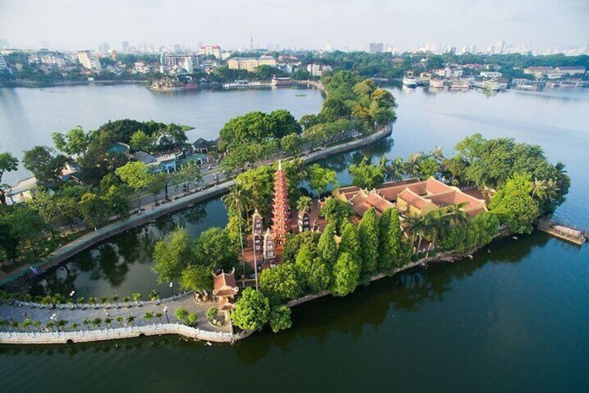 An aerial view of a riverside park with a pagoda, a bridge, and a cityscape in the background. 1