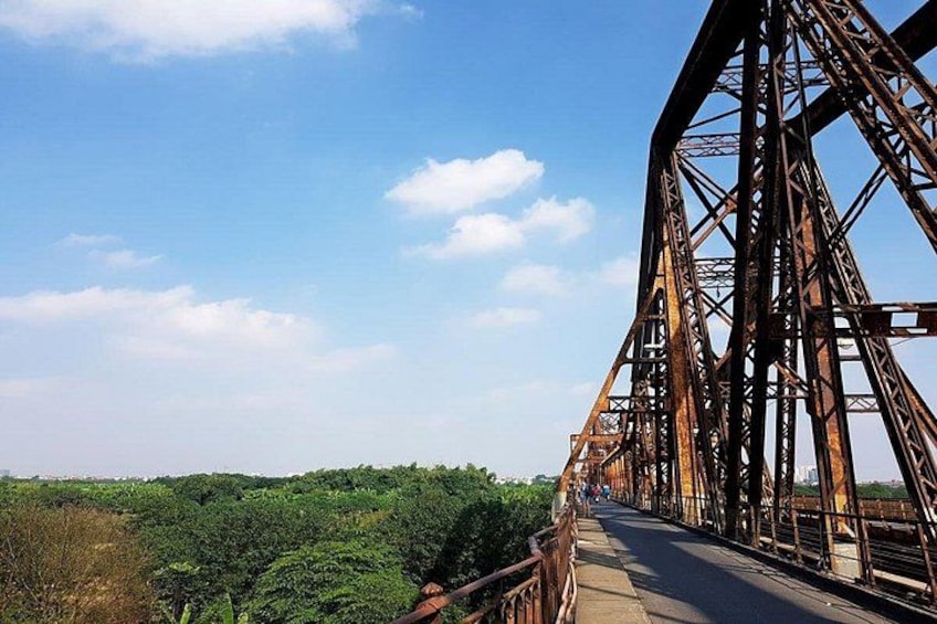 A steel bridge with a metal railing, surrounded by greenery and a clear sky. 5