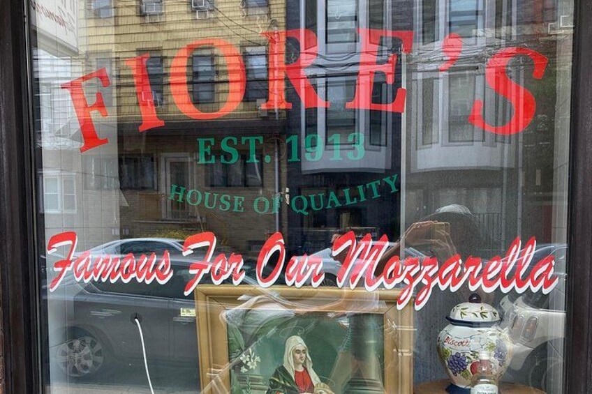 A storefront with the sign 'FIORE'S EST. 1913 HOUSE OF QUALITY' and a display of a ceramic jar with a label. 2